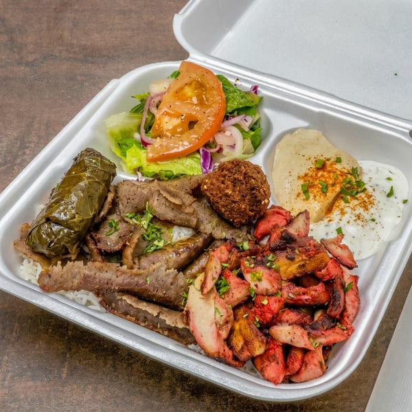 A takeout container filled with rice, gyro meat, chicken, falafel, stuffed grape leaf, salad, hummus, and tzatziki.
