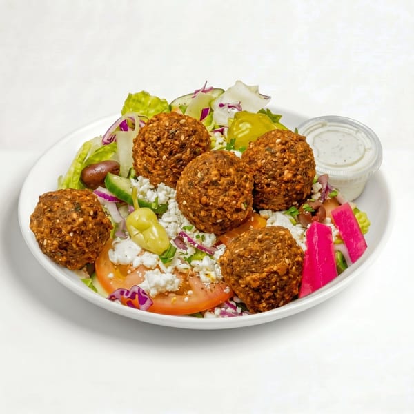 Falafel salad with lettuce, tomatoes, feta, olives, pickled vegetables, and a side of dressing.