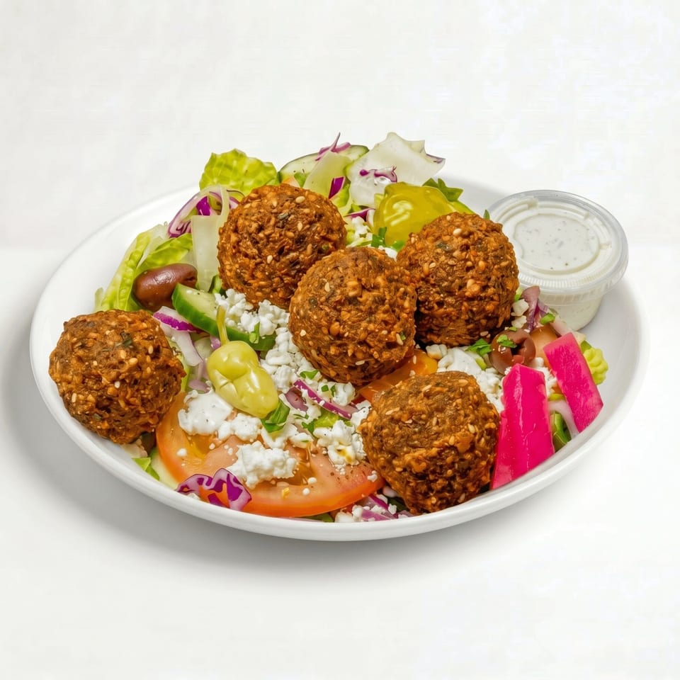 Falafel salad with lettuce, tomatoes, feta, olives, pickled vegetables, and a side of dressing.