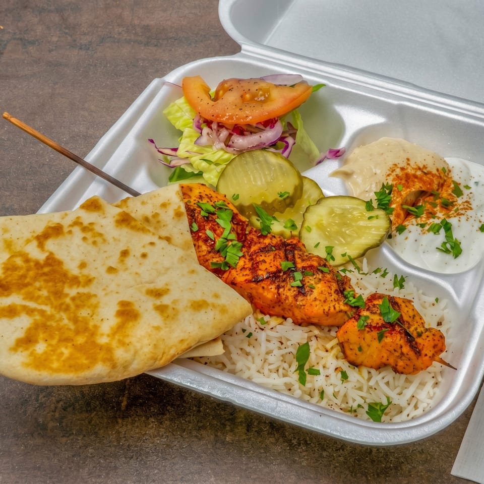 Chicken shish tawook skewer with rice, pita bread, salad, pickles, hummus, and garlic sauce.